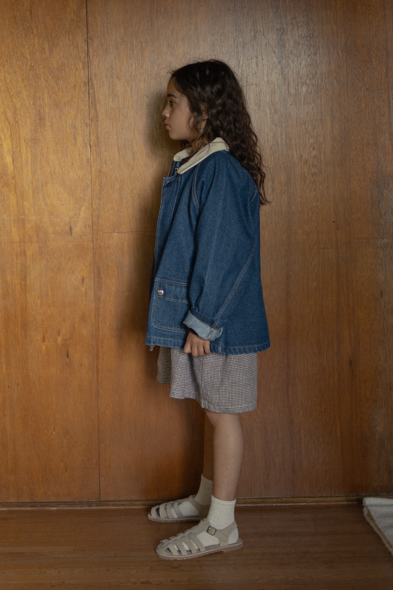 Child wearing the Brooks Jacket in Indigo by Gillian Stevens, side view against warm wood panelling