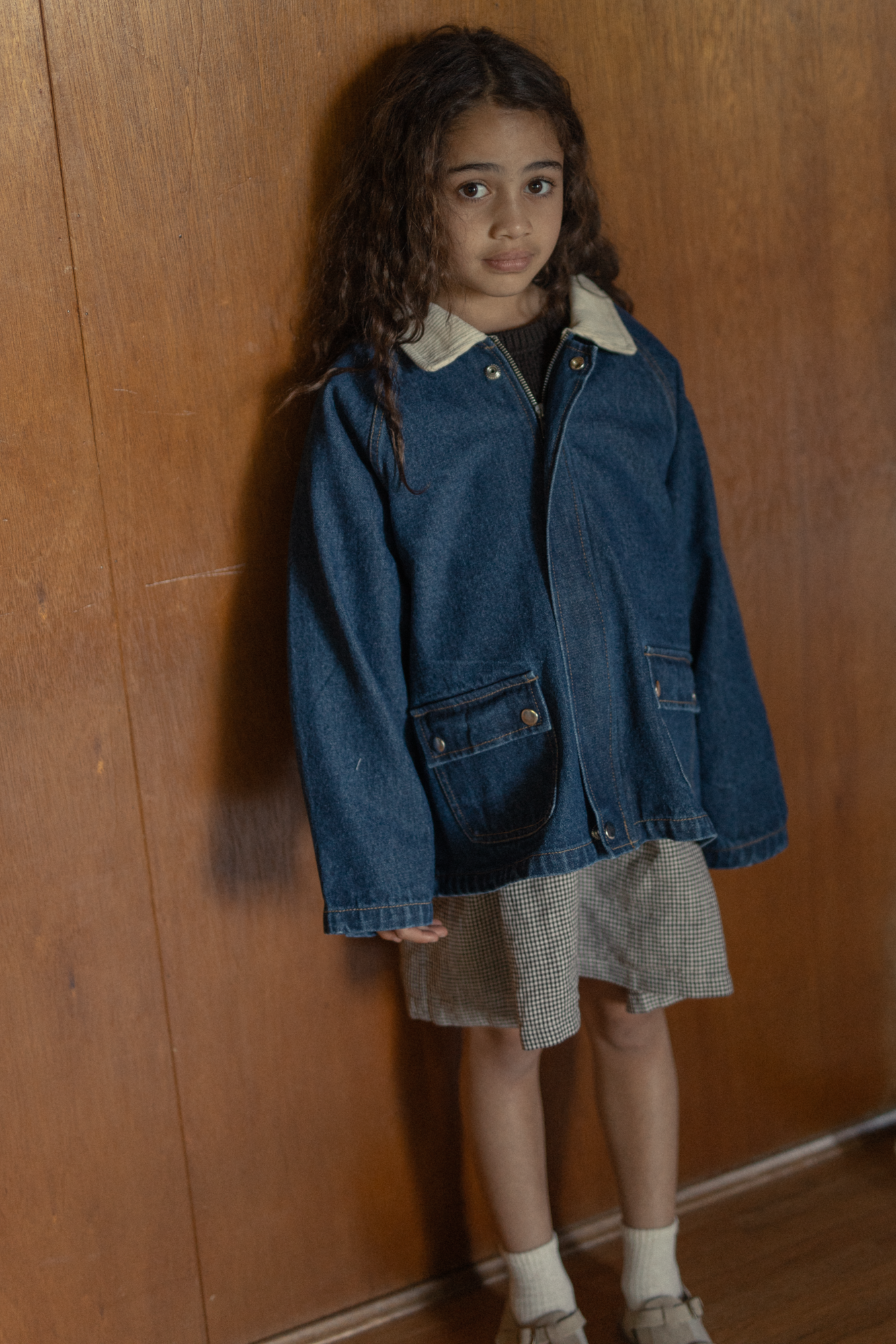 Child wearing the Brooks Jacket in Indigo by Gillian Stevens, front view against a warm wood-panelled wall