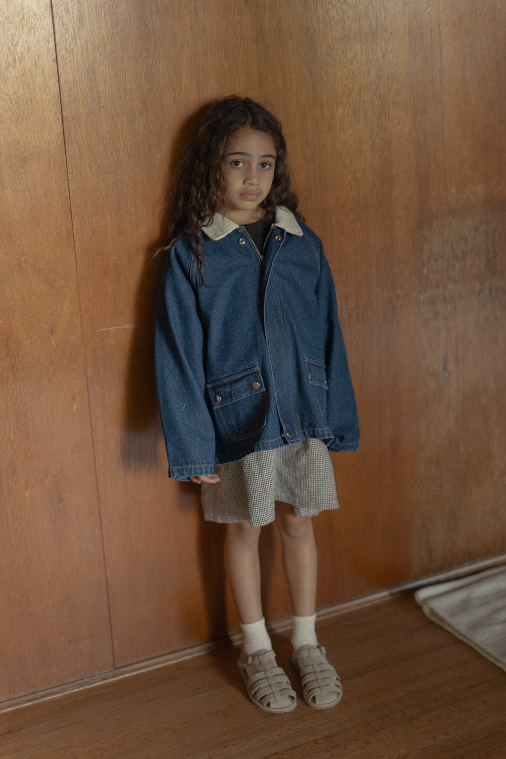 Child wearing the Brooks Jacket in Indigo by Gillian Stevens, full-length front view against a timber wall
