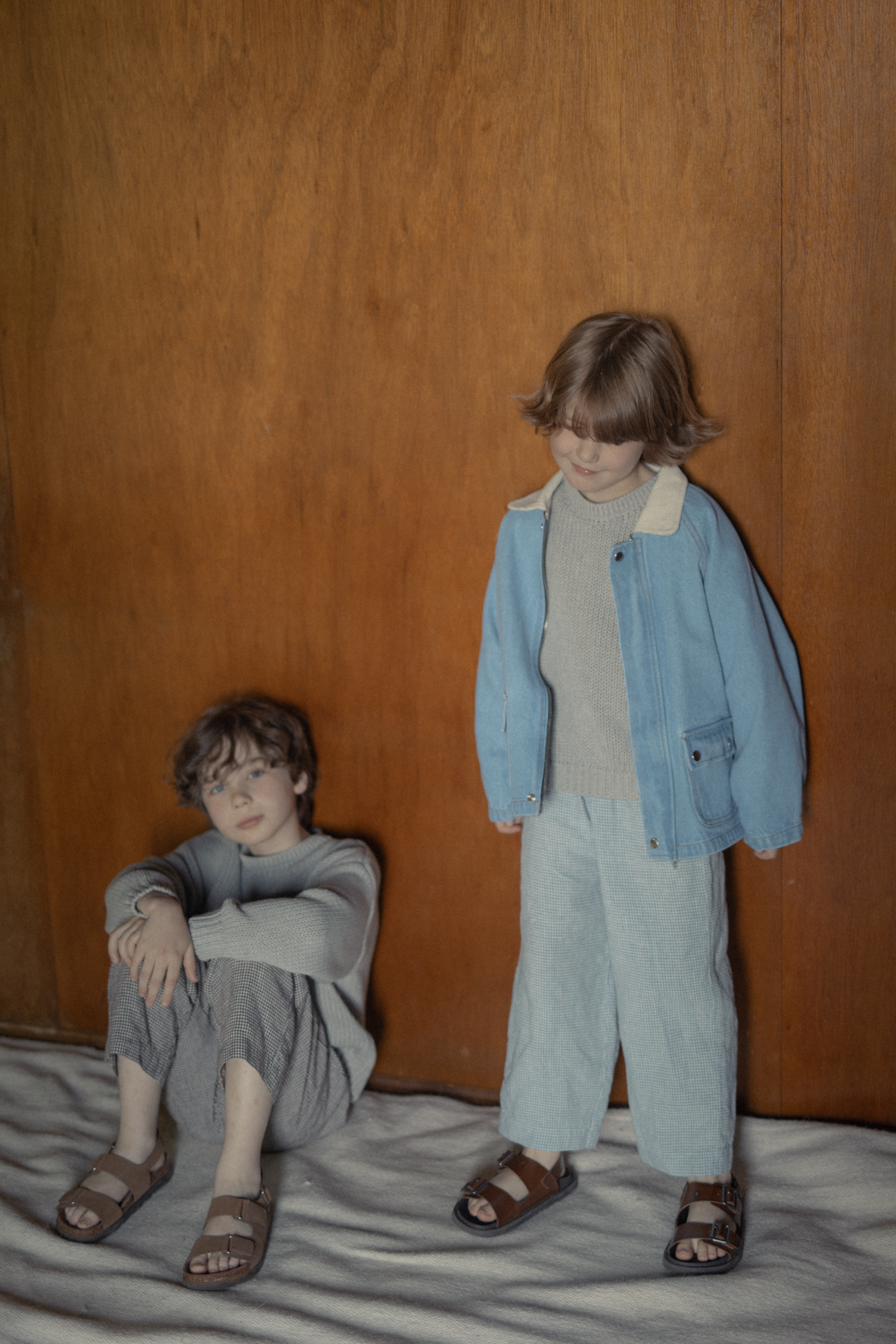 Two children styled in the Brooks Jacket Vintage Blue by Gillian Stevens, against a warm timber wall