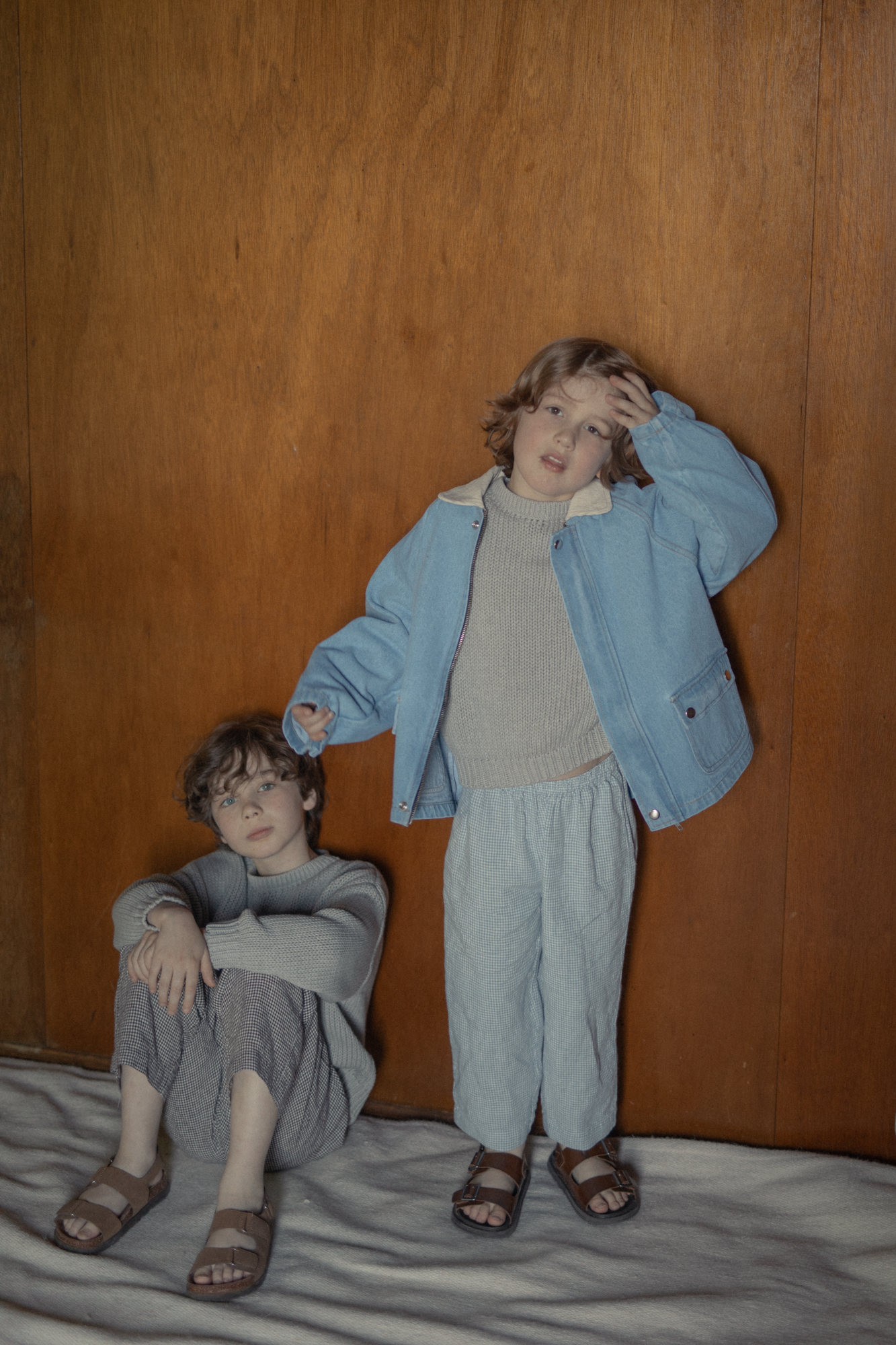 Two children styled with the Brooks Jacket in Vintage Blue by Gillian Stevens, front view against a wood-panelled wall
