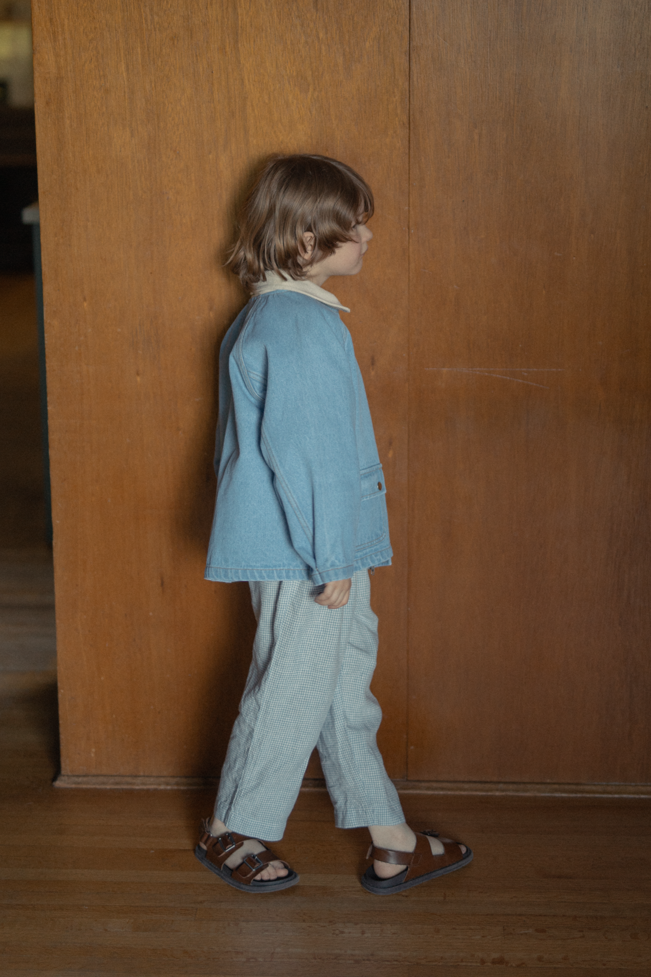 Child wearing the Brooks Jacket in Vintage Blue by Gillian Stevens, side view against warm timber panelling