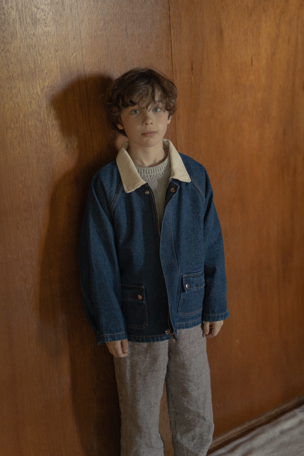 Child wearing the Brooks Jacket in Indigo by Gillian Stevens, front view against a warm timber wall