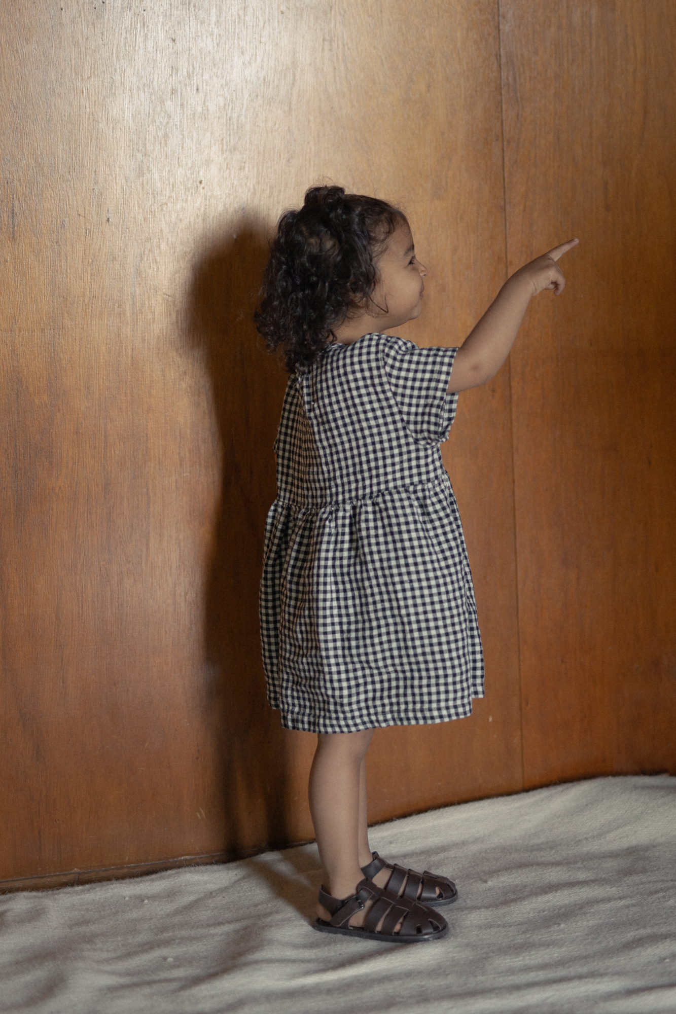 Child wearing the Mini Aya in Gingham Noir by Gillian Stevens, back view showing tiered skirt detail