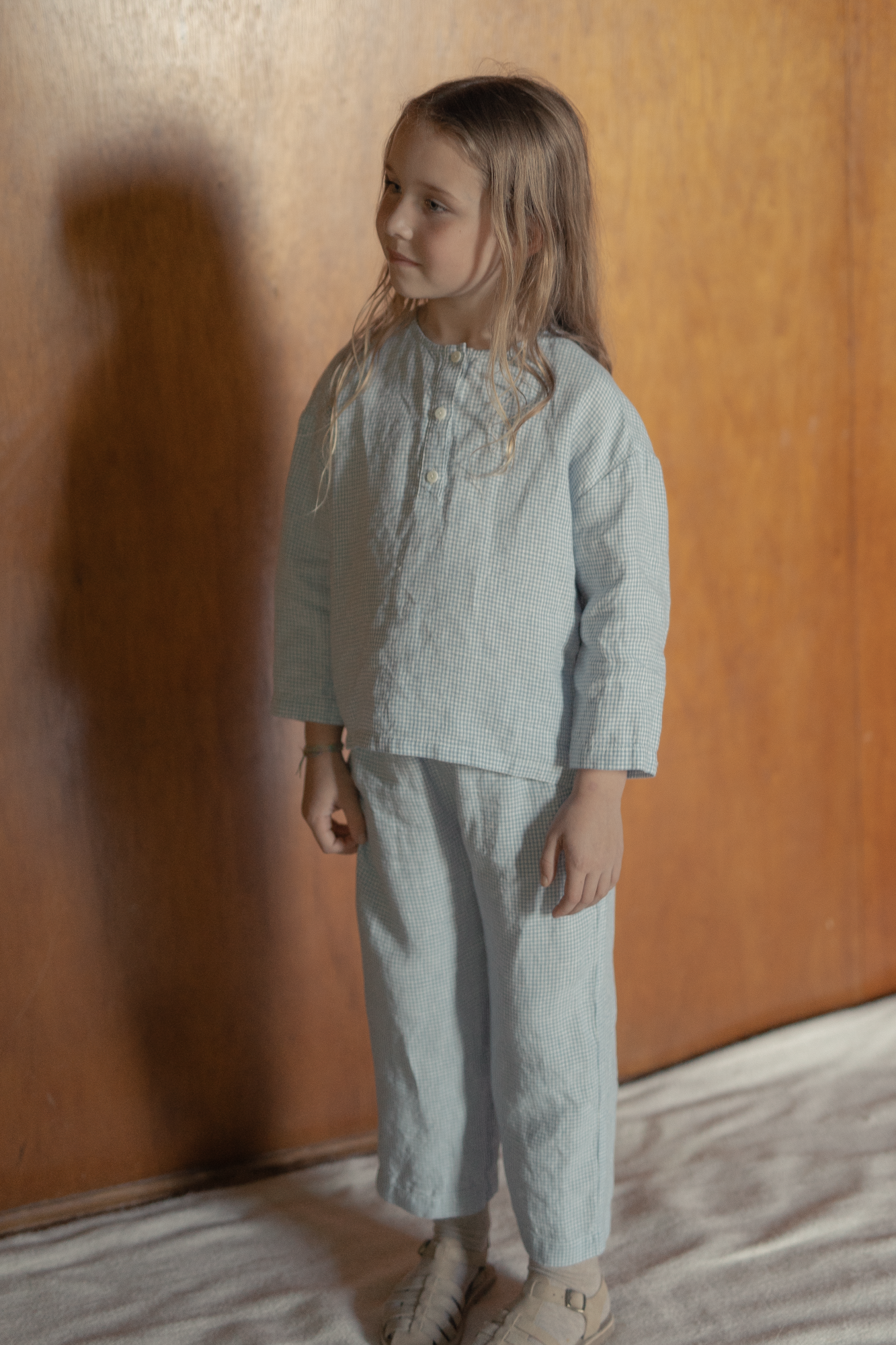 Child wearing the Bertie Top in Pale Blue Gingham by Gillian Stevens, front three-quarter view styled with matching pants