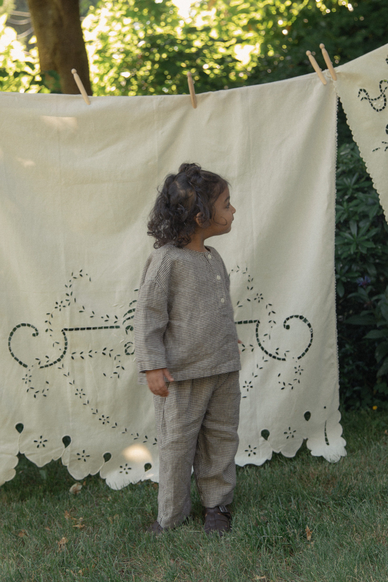 Child wearing the Bertie Pant in Espresso Gingham by Gillian Stevens, side view in a garden setting