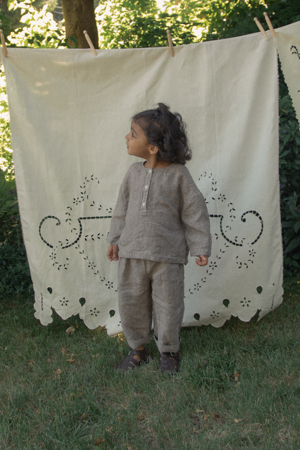 Child wearing the Bertie Pant in Espresso Gingham by Gillian Stevens, front view in a garden setting