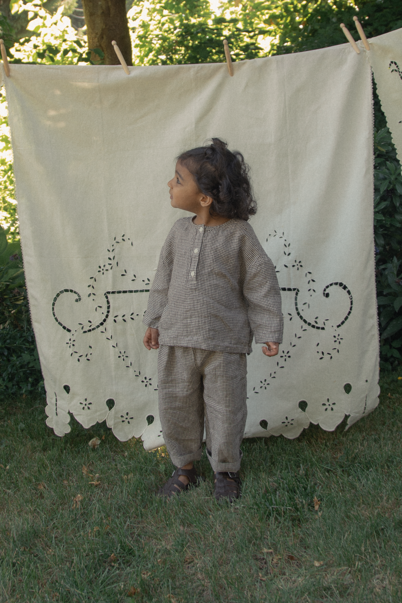 Child wearing the Bertie Pant in Espresso Gingham by Gillian Stevens, front view in a garden setting