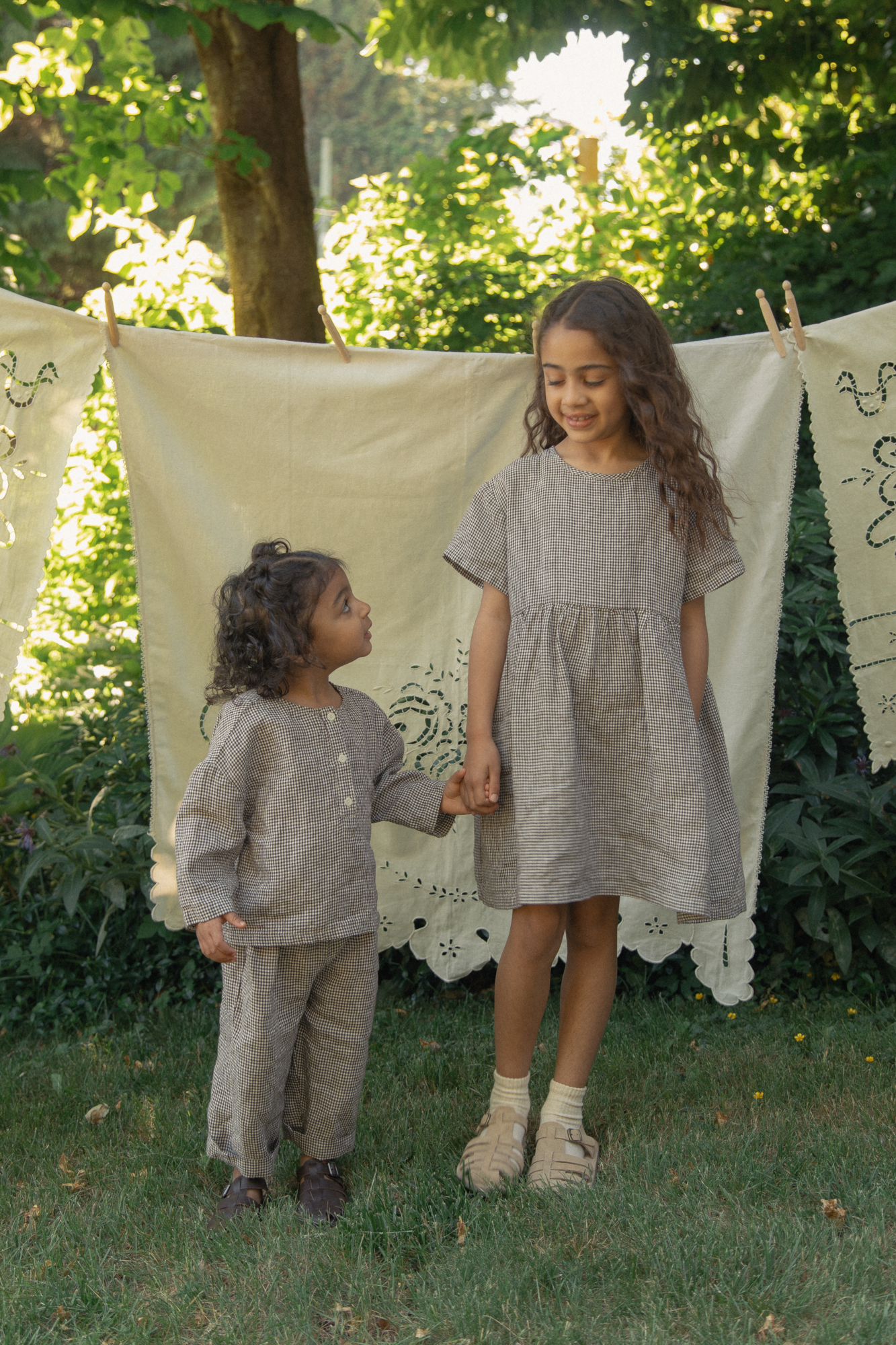 Two children outdoors in Espresso Gingham by Gillian Stevens, older child in the Bertie Top styled as a dress
