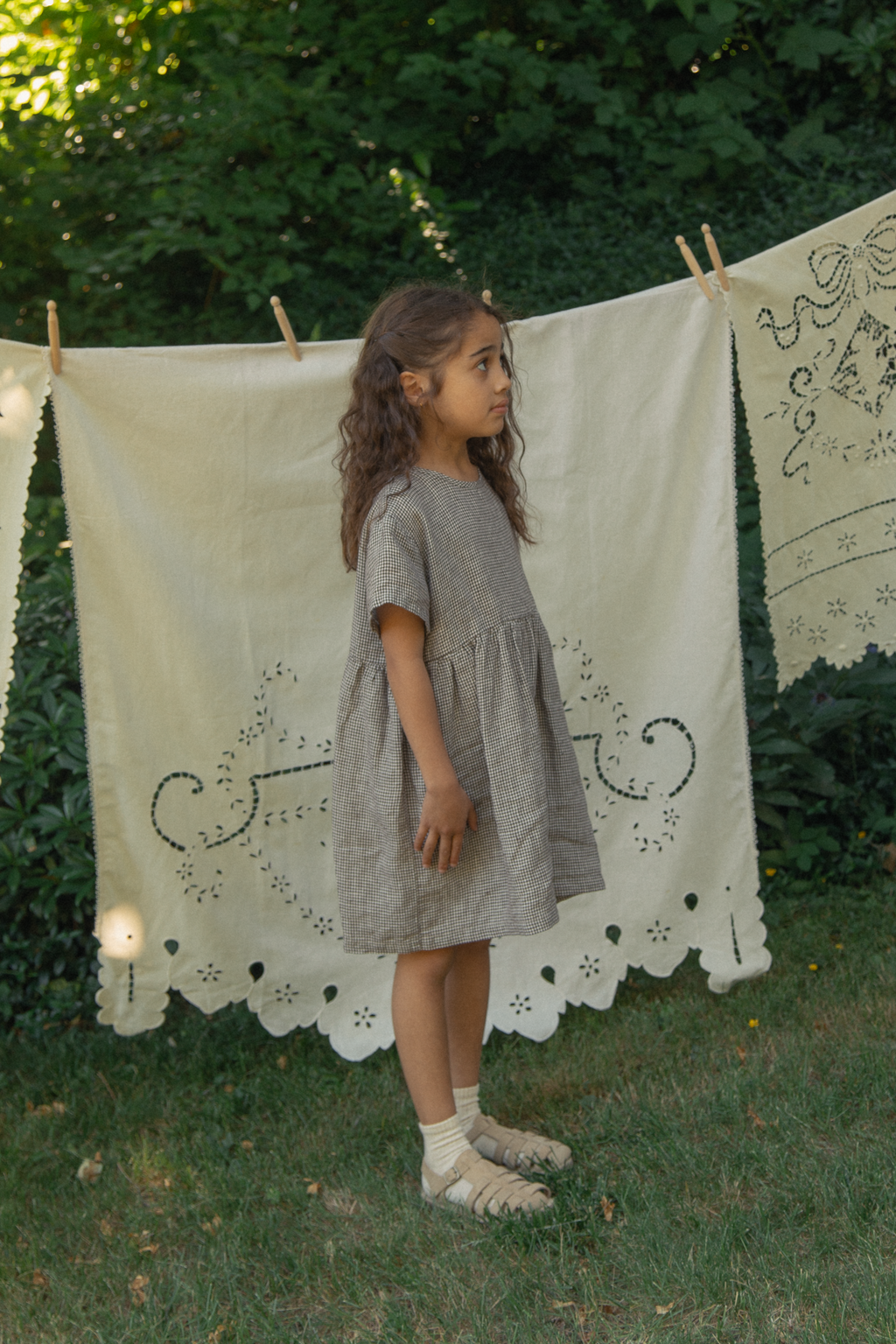 Child wearing the Mini Aya in Espresso Gingham by Gillian Stevens, side view outdoors