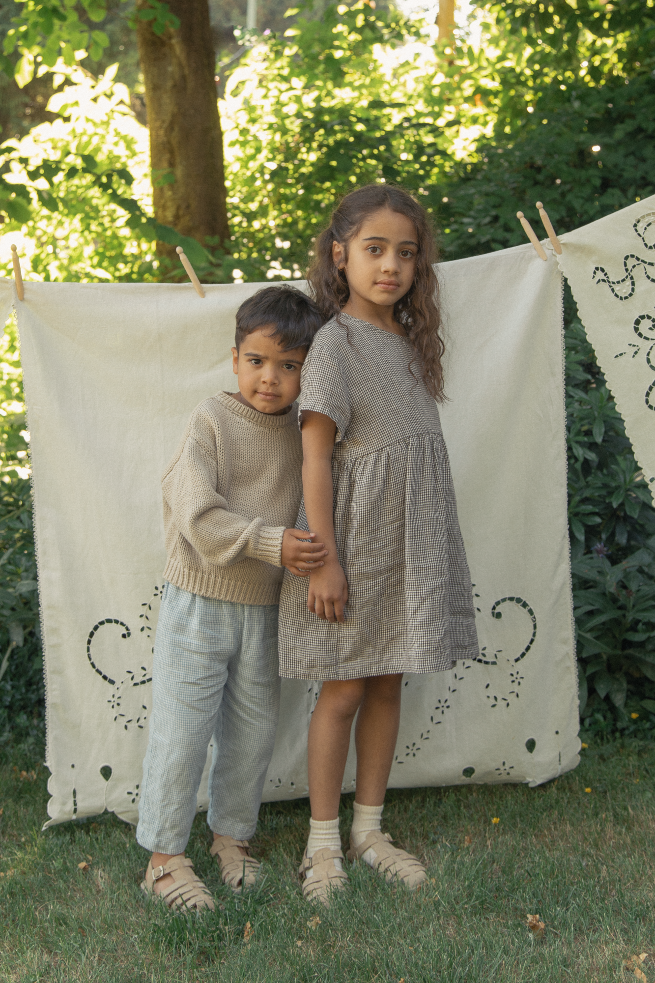Child wearing the Mini Aya in Espresso Gingham by Gillian Stevens, front view in a garden setting