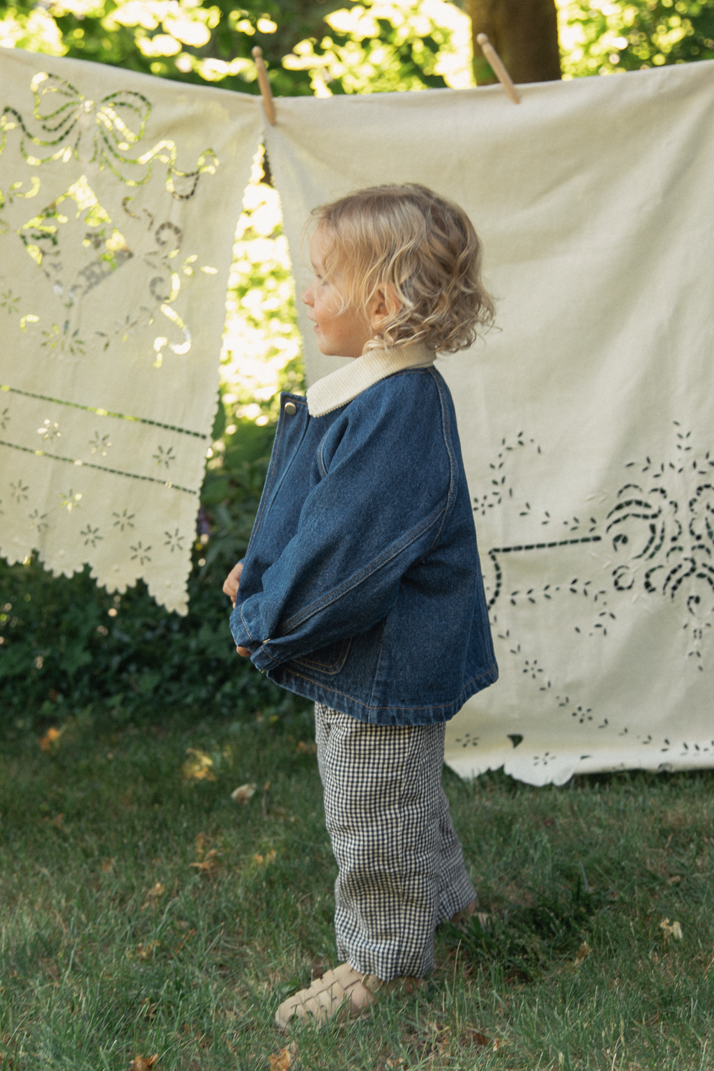 Child wearing the Brooks Jacket in Indigo by Gillian Stevens, side view outdoors with linen on a clothesline