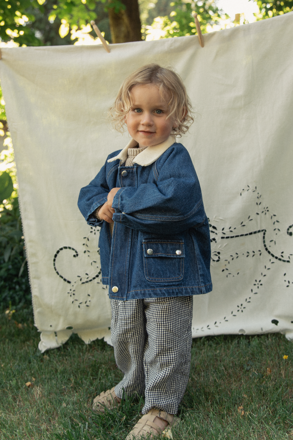 Child wearing the Brooks Jacket in Indigo by Gillian Stevens, front view styled outdoors with gingham trousers
