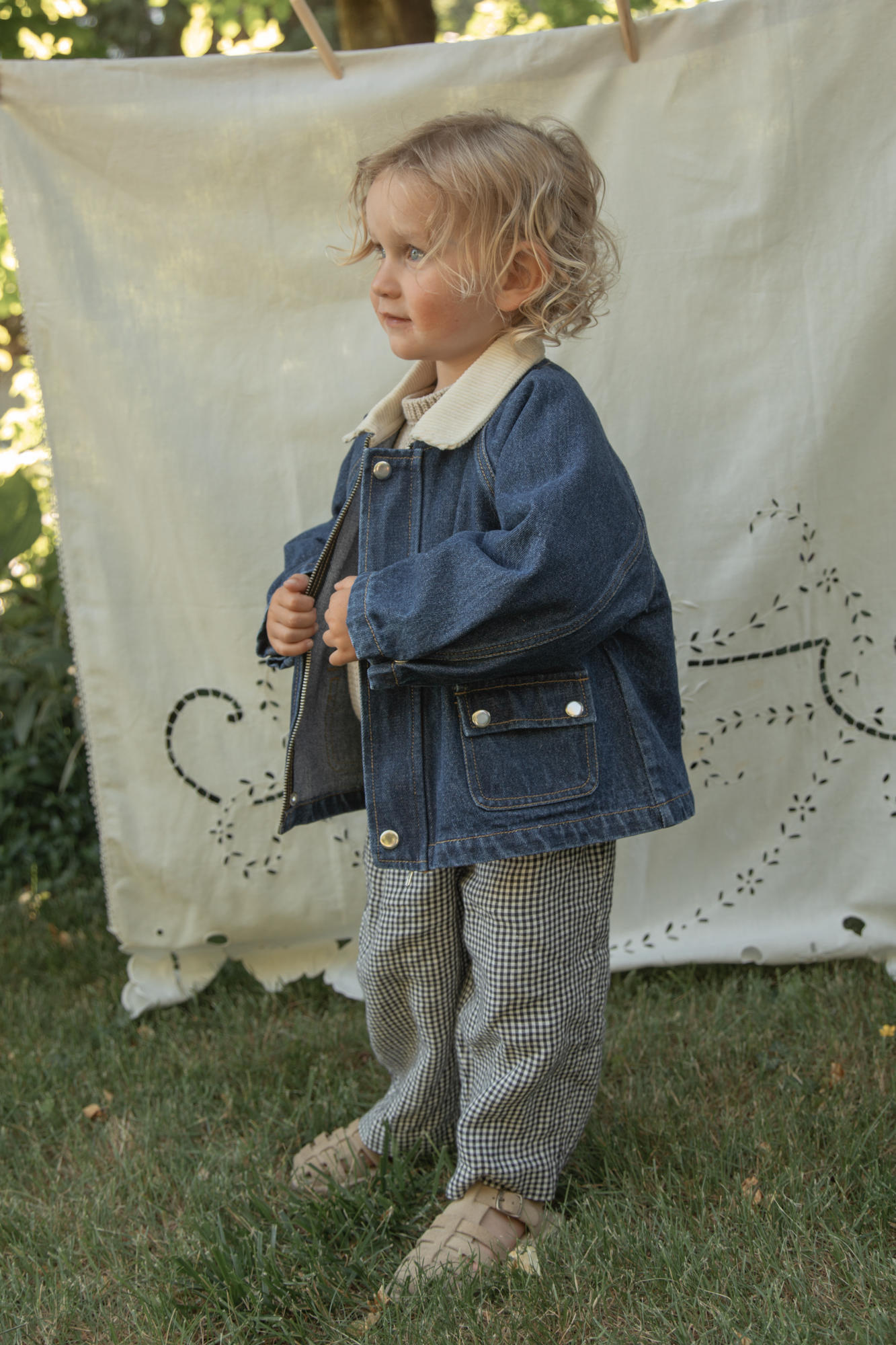 Child wearing the Brooks Jacket in Indigo by Gillian Stevens, side view outdoors with jacket held open