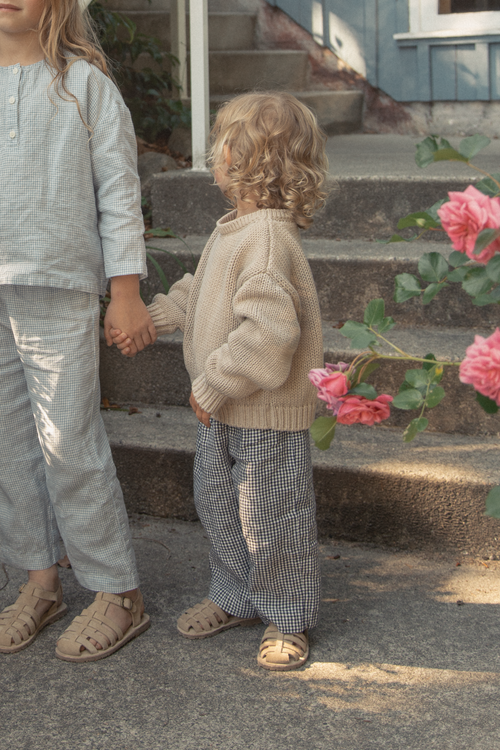 Child wearing the Bertie Pant in Marine Gingham by Gillian Stevens, back view styled with a knit sweater outdoors