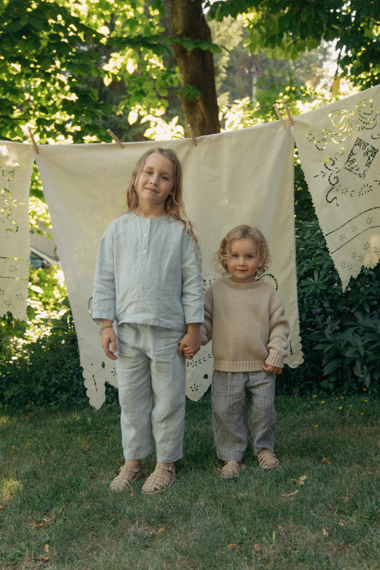 Child wearing the Bertie Pant in Marine Gingham by Gillian Stevens, styled with a knit sweater in a garden setting
