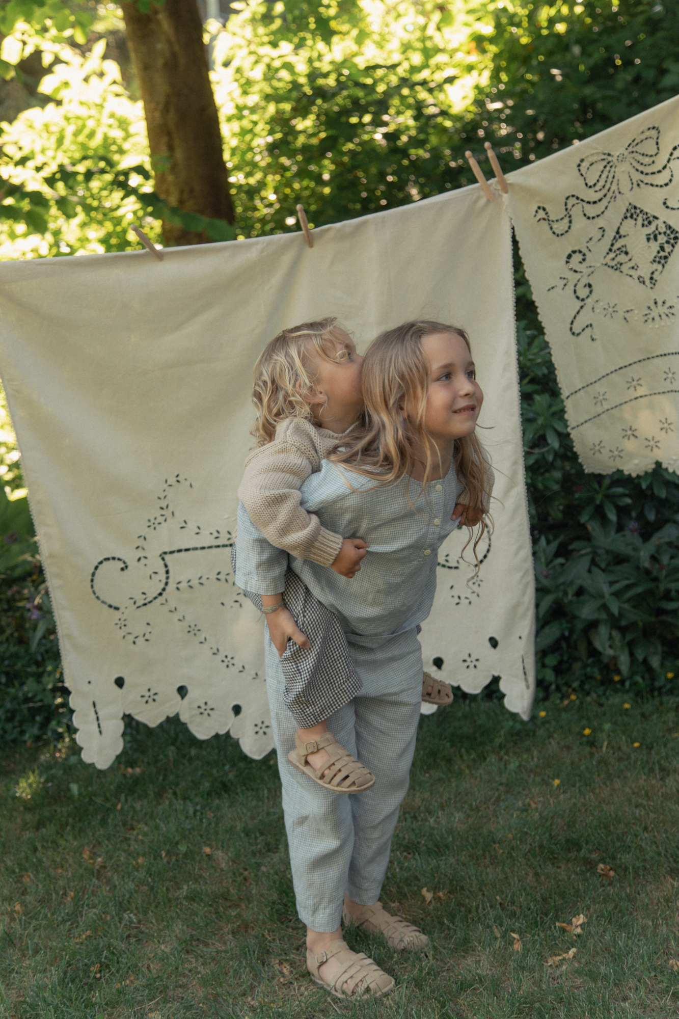 Child wearing the Bertie Pant in Pale Blue Gingham by Gillian Stevens, front view in a garden setting