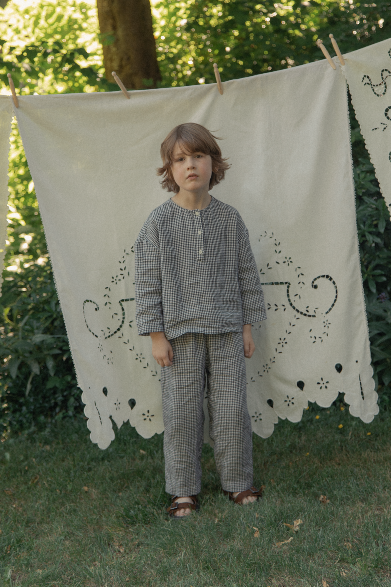 Child wearing the Bertie Top in Marine Gingham by Gillian Stevens, front view in a garden setting