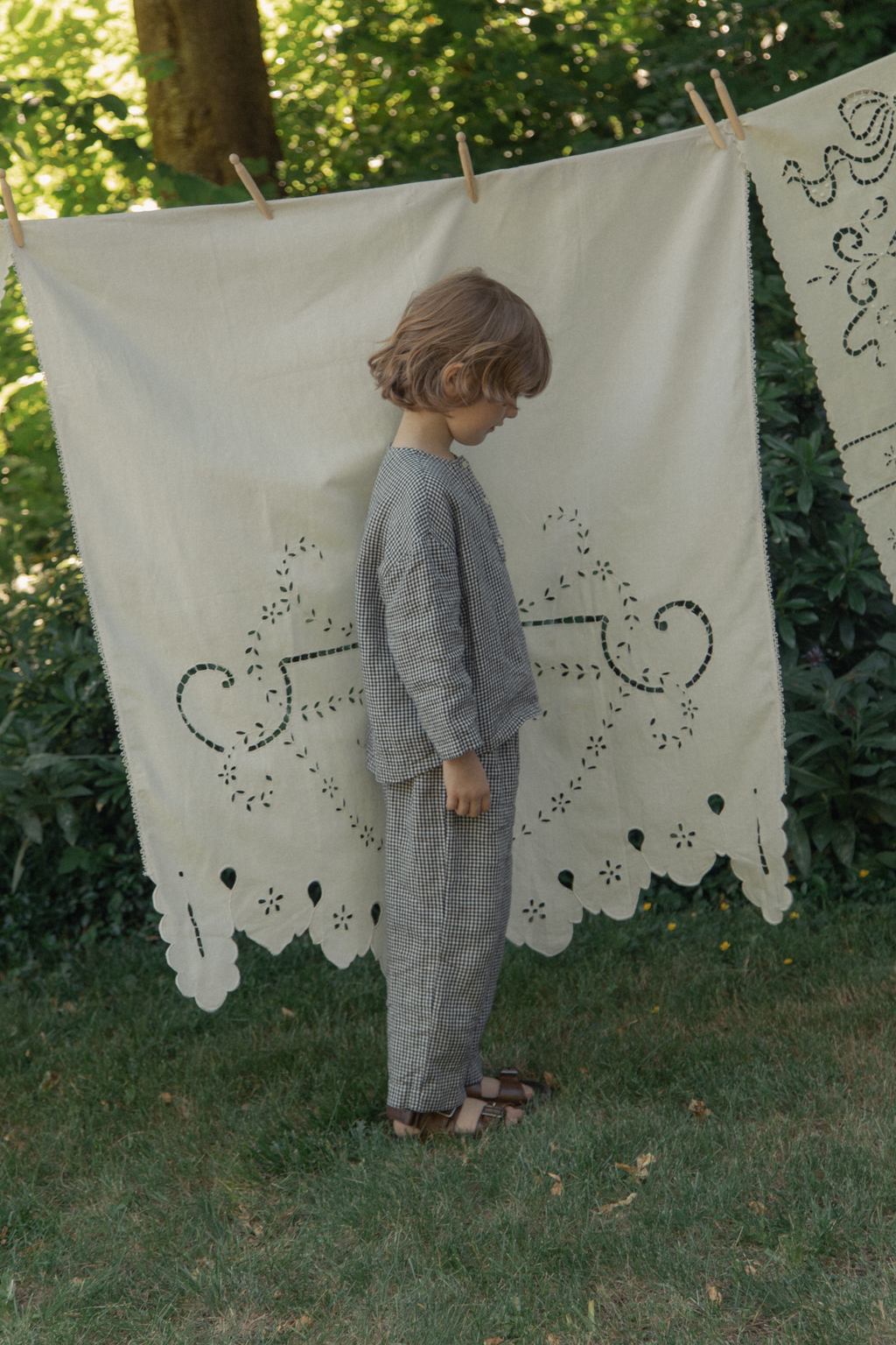 Child wearing the Bertie Top in Marine Gingham by Gillian Stevens, side view in a garden setting