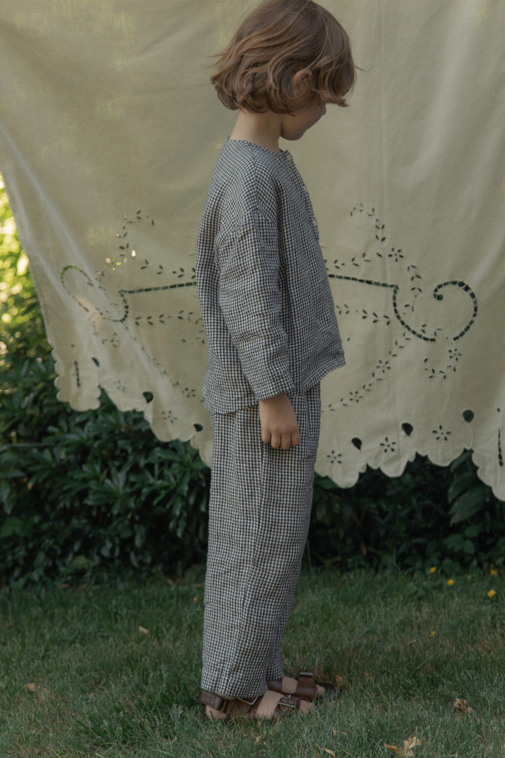 Child wearing the Bertie Pant in Marine Gingham by Gillian Stevens, side view styled with matching top outdoors