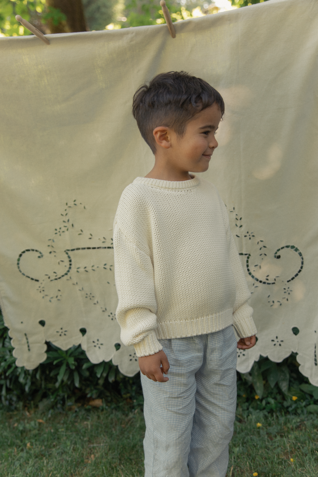Child wearing the Mini Townes Pullover in Alabaster by Gillian Stevens, three-quarter view outdoors
