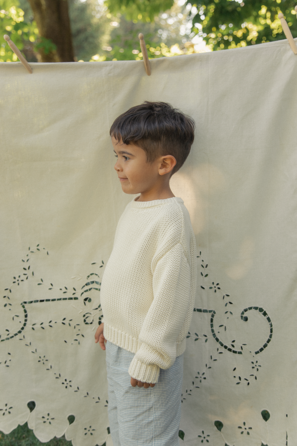 Child wearing the Mini Townes Pullover in Alabaster by Gillian Stevens, side view outdoors