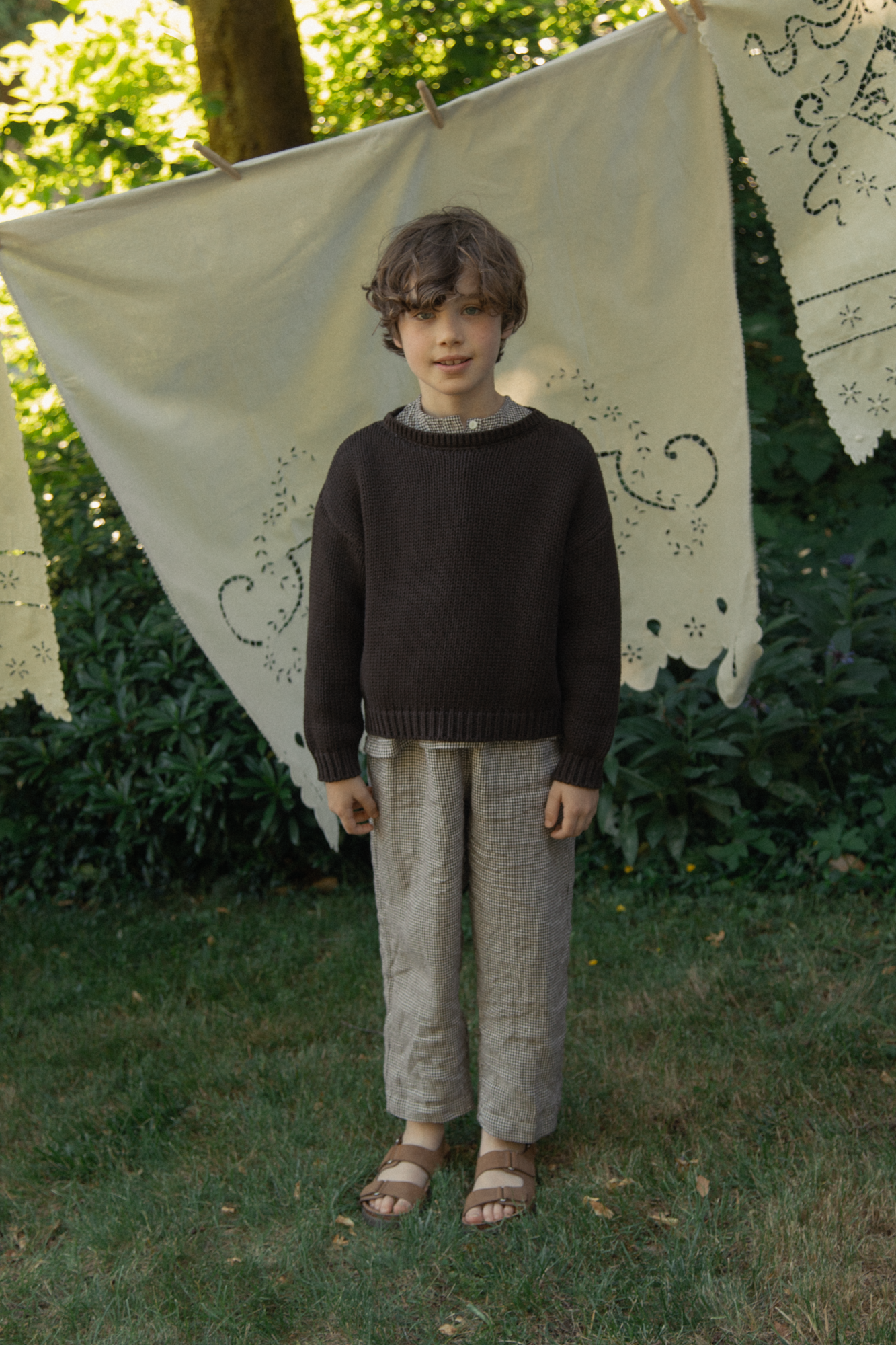 Child wearing the Bertie Pant in Espresso Gingham by Gillian Stevens, full-length front view in a garden setting