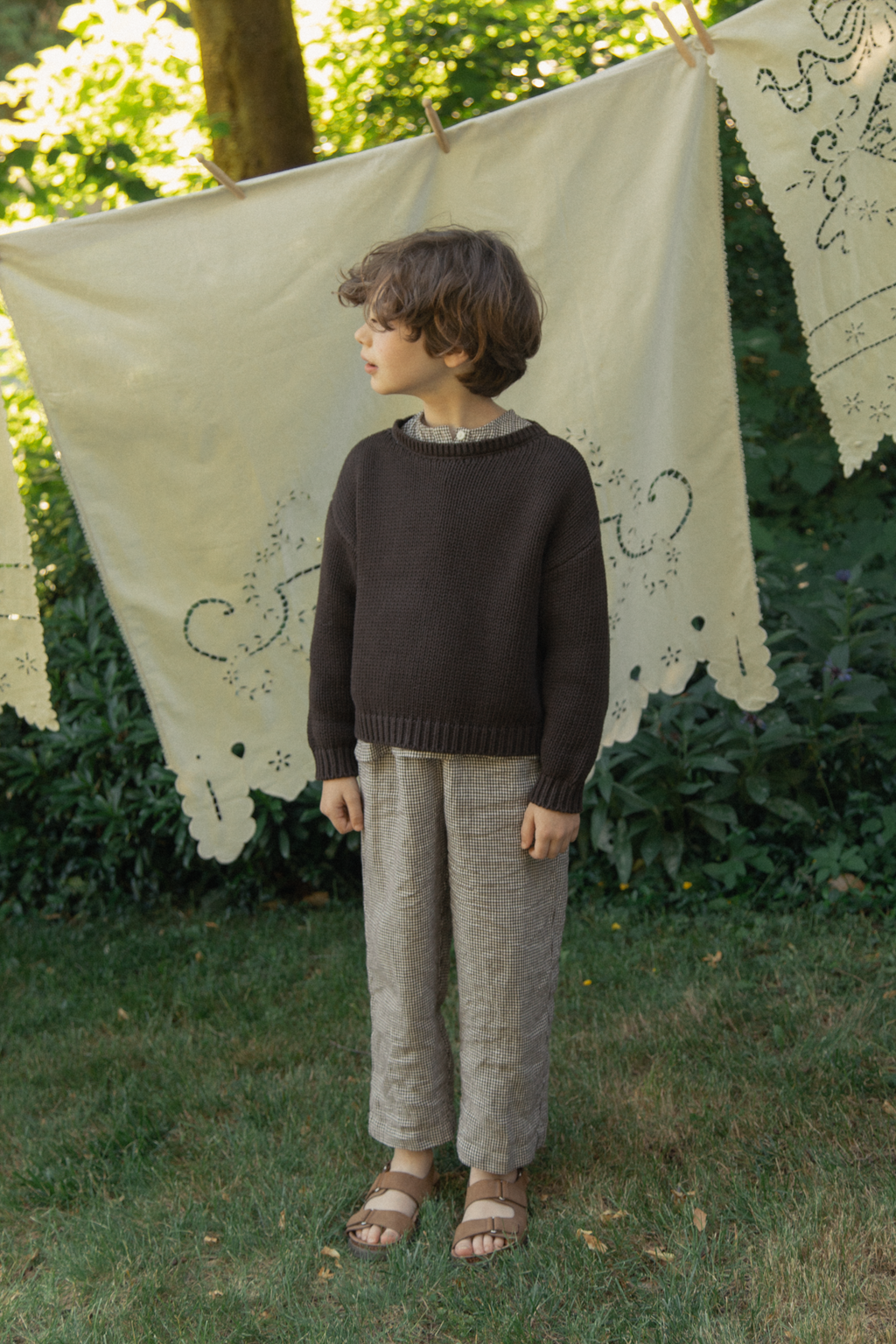 Child wearing the Mini Townes Pullover in Espresso by Gillian Stevens, full-length outdoor garden setting