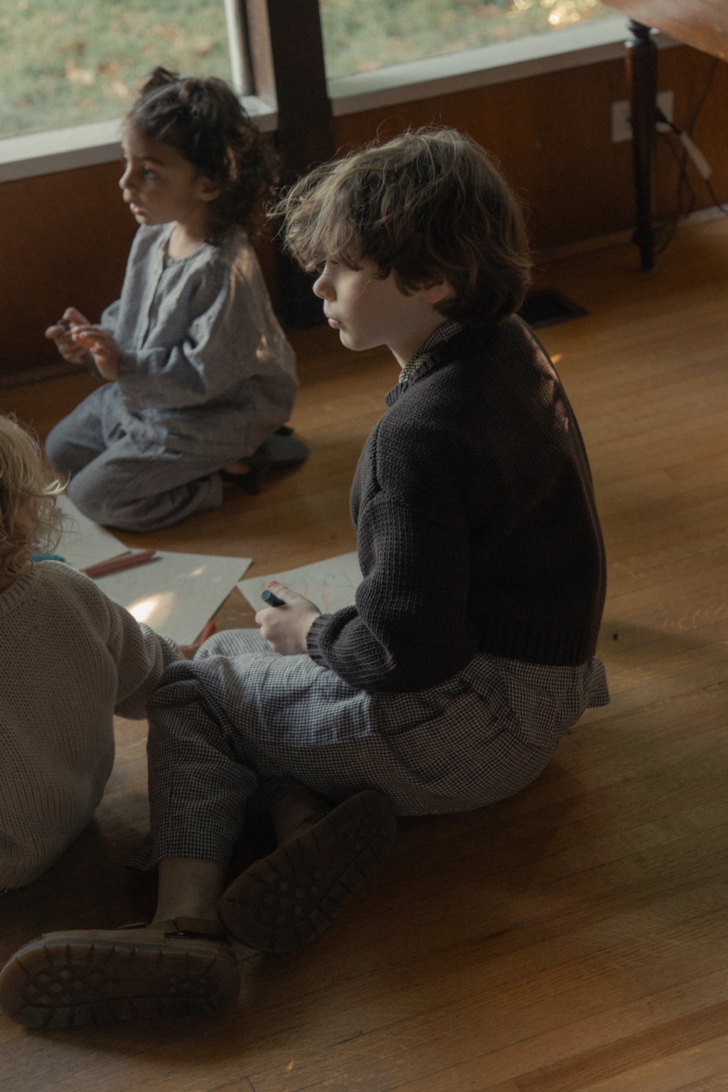 Child wearing the Mini Townes Pullover in Espresso by Gillian Stevens, side view seated on wooden floor