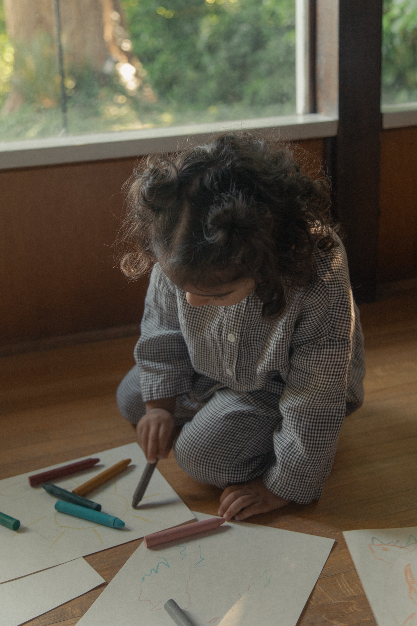 Child wearing the Bertie Top in Espresso Gingham by Gillian Stevens, seated on floor drawing with crayons