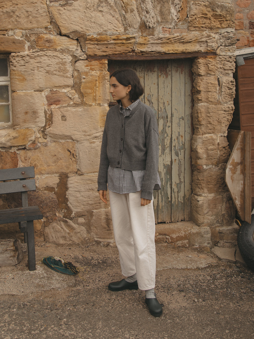 Model wearing the Giséle Cardigan in Charcoal by Gillian Stevens, side view against rustic stone wall