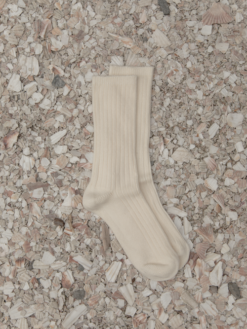 The Allen Sock in Ivory by Gillian Stevens, flat-lay pair on crushed shell surface