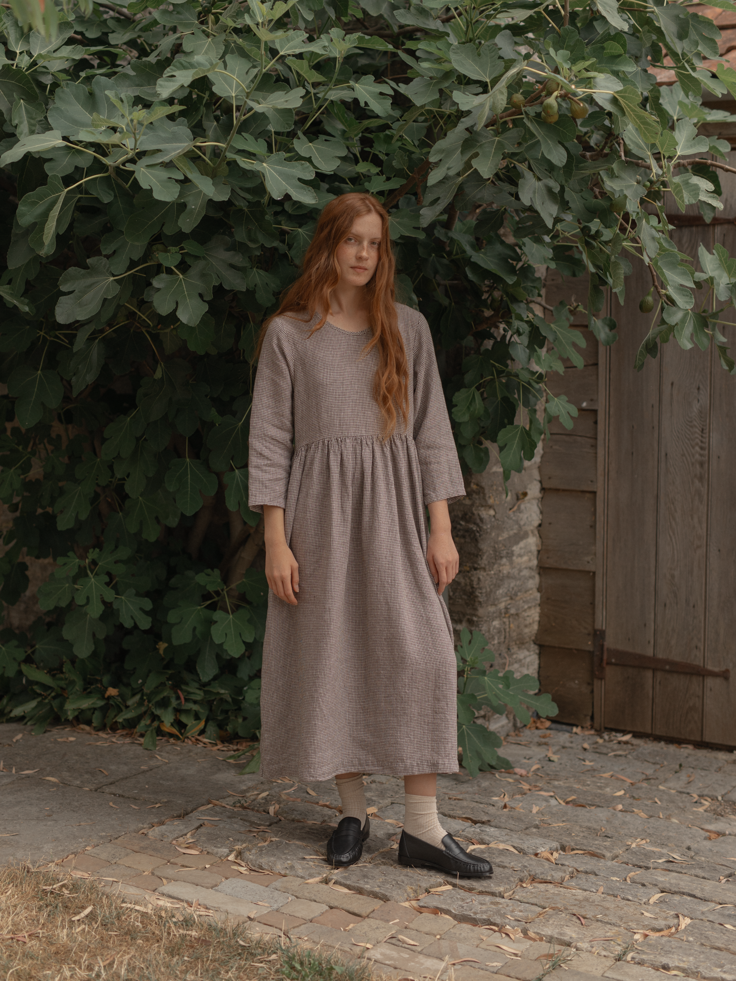 Model wearing the Artie Dress in Espresso Gingham by Gillian Stevens, front view outdoors by a fig tree