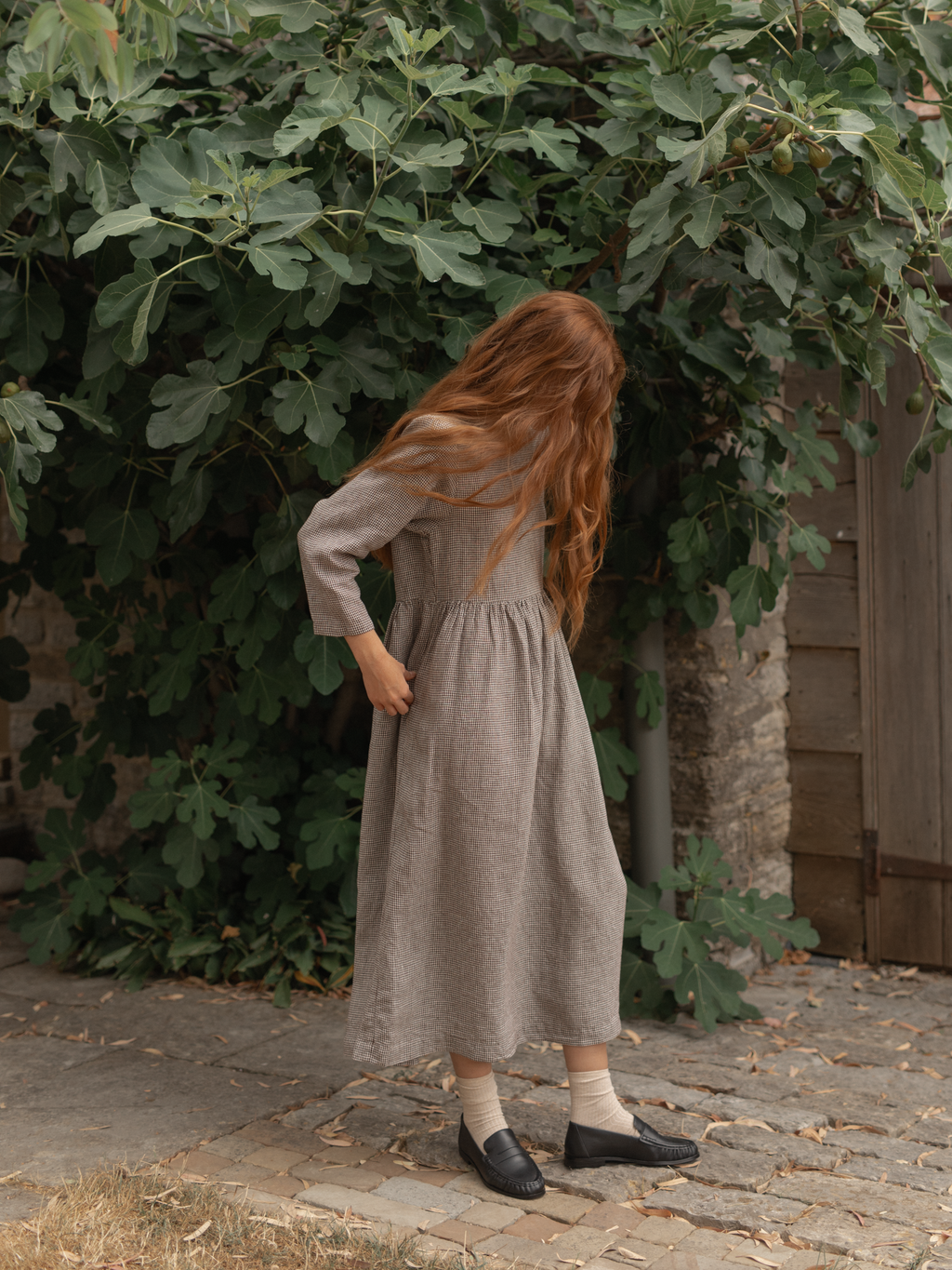 Model wearing the Artie Dress in Espresso Gingham by Gillian Stevens, back view on cobblestone path