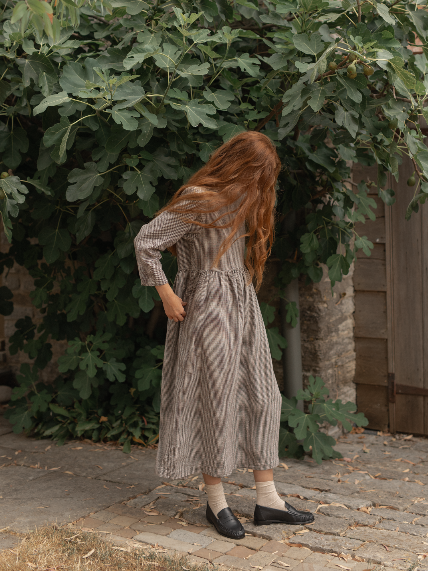 Model wearing the Artie Dress in Espresso Gingham by Gillian Stevens, back view on cobblestone path