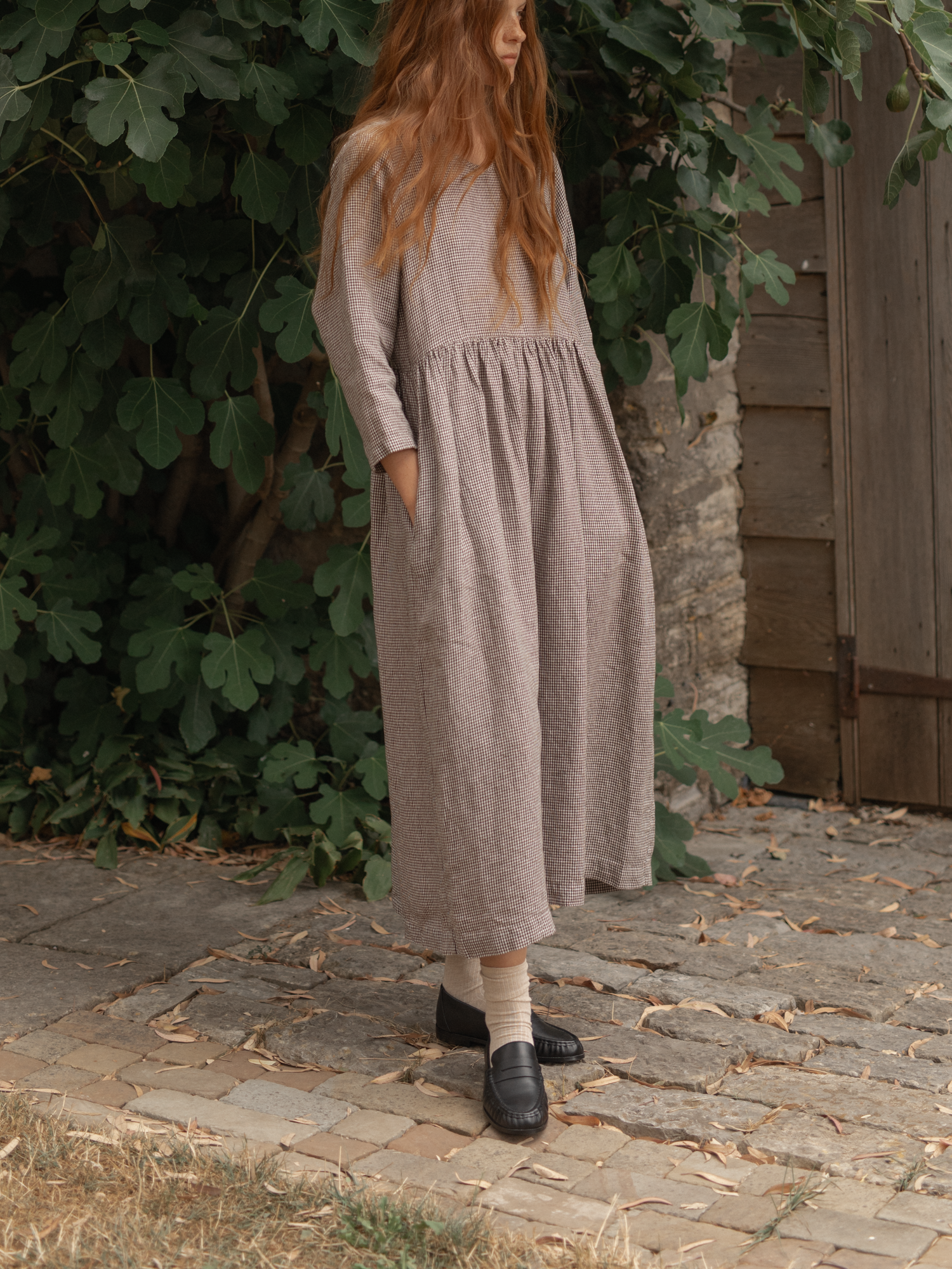 Model wearing the Artie Dress in Espresso Gingham by Gillian Stevens, side view on cobblestone outdoors