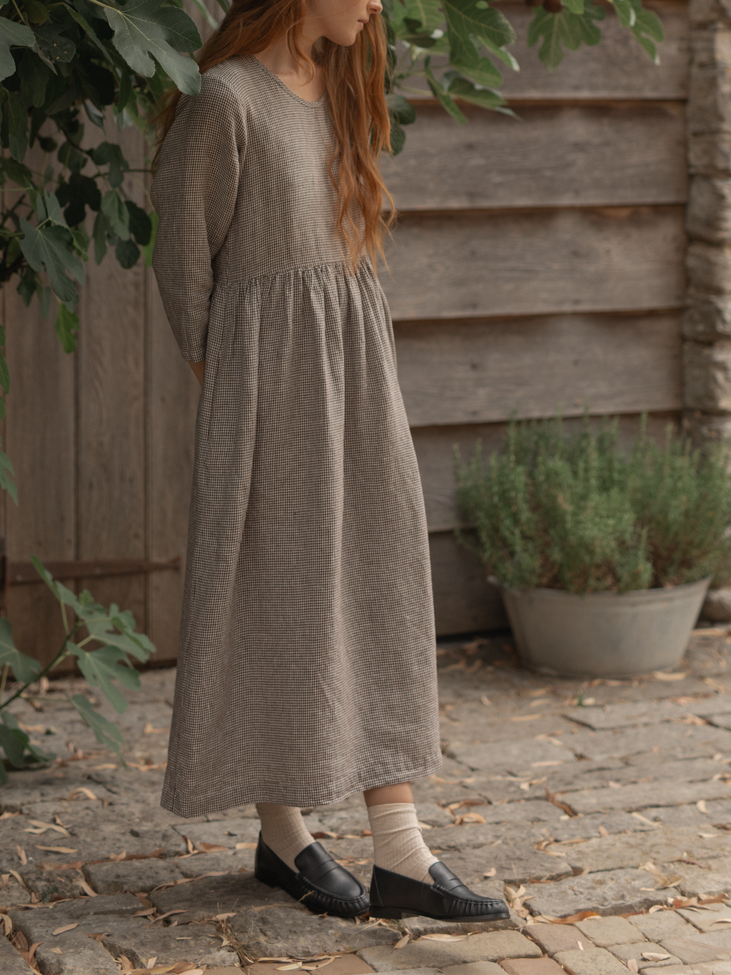 Model wearing the Artie Dress in Espresso Gingham by Gillian Stevens, side view on cobblestone outdoor setting