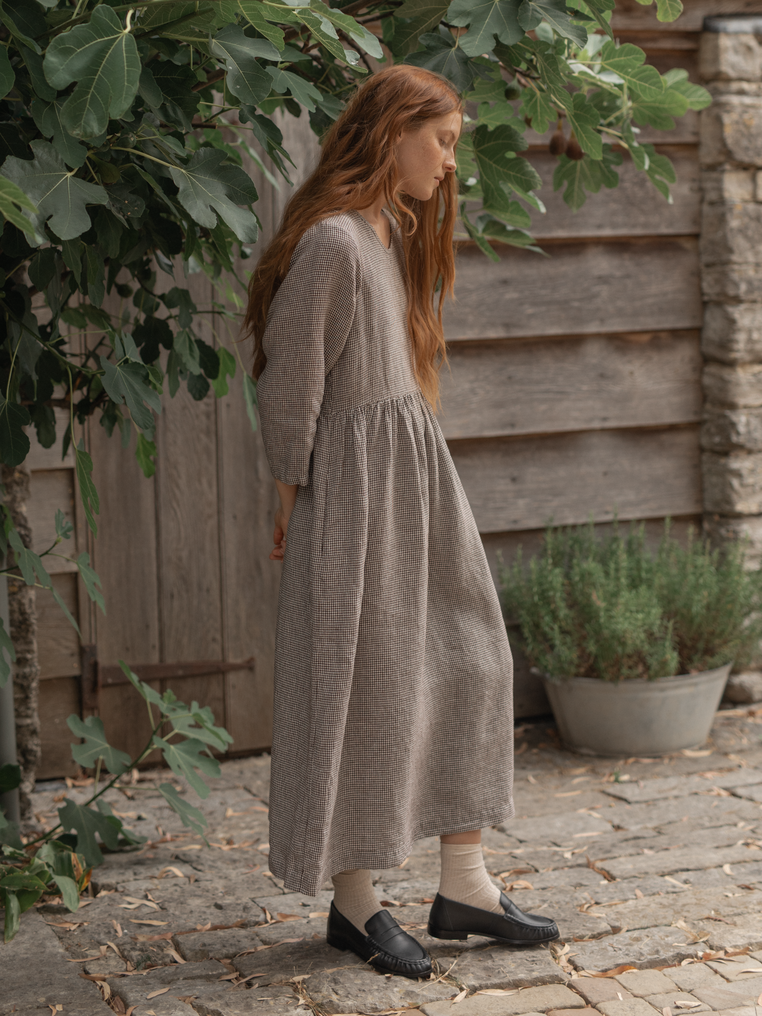 Model wearing the Artie Dress in Espresso Gingham by Gillian Stevens, side view outdoors on cobblestones