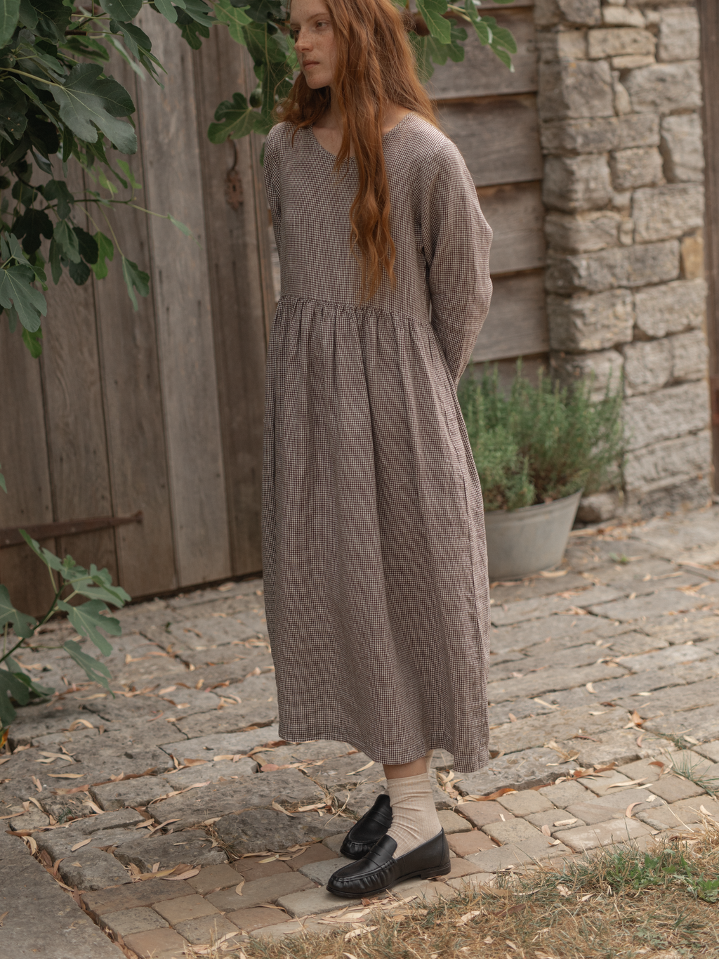 Model wearing the Artie Dress in Espresso Gingham by Gillian Stevens, three-quarter view on cobblestone