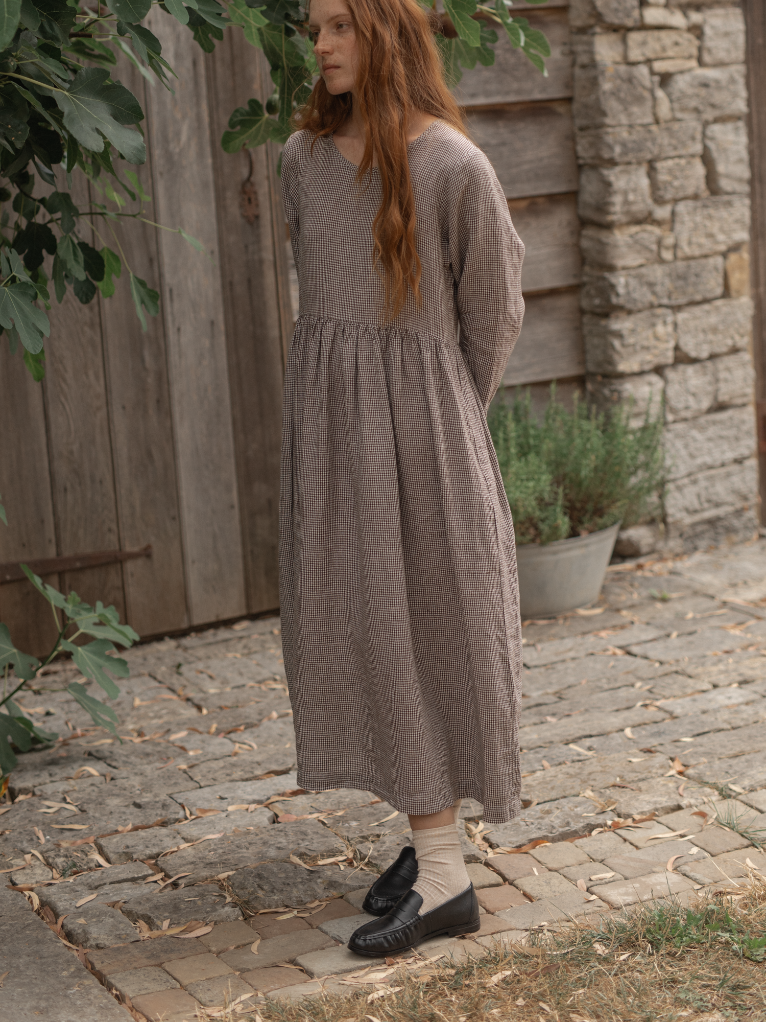 Model wearing the Artie Dress in Espresso Gingham by Gillian Stevens, three-quarter view on cobblestone