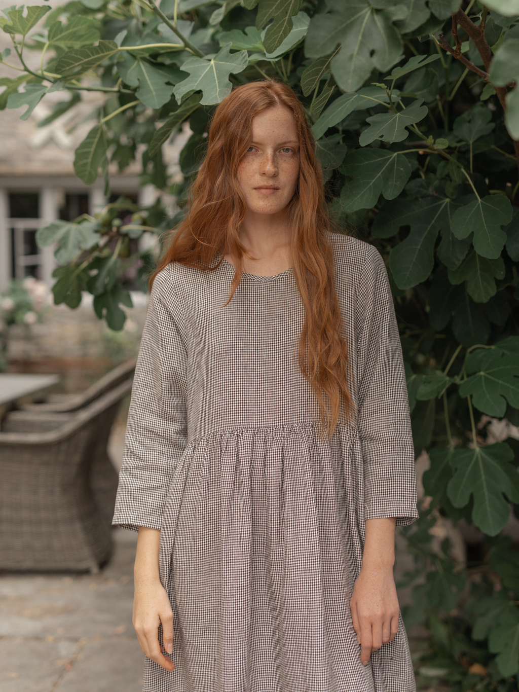 Model wearing the Artie Dress in Espresso Gingham by Gillian Stevens, front view among fig tree foliage