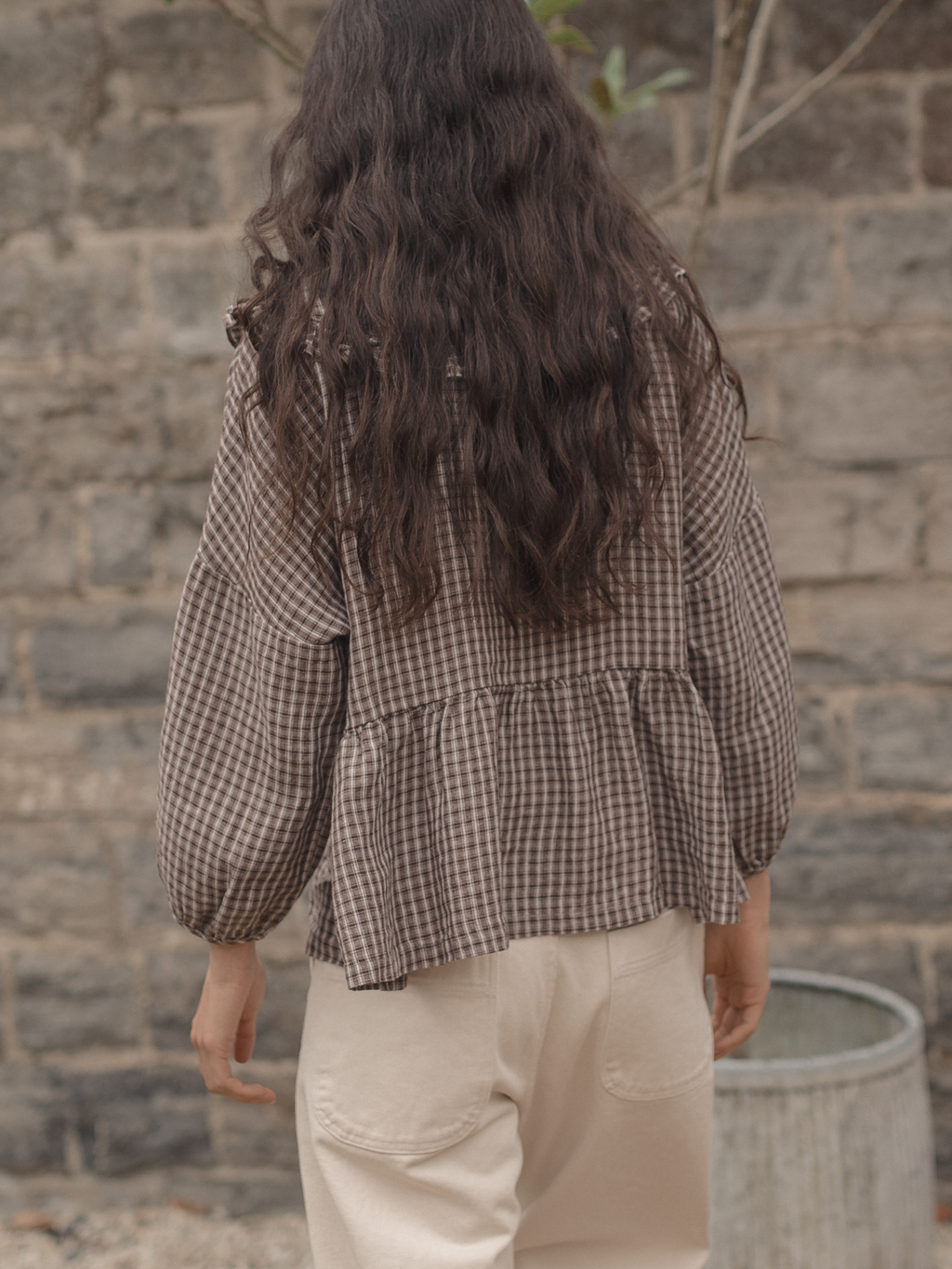 Model wearing the Winsley Blouse in Chocolate Plaid by Gillian Stevens, back view showing tiered hem and balloon sleeves