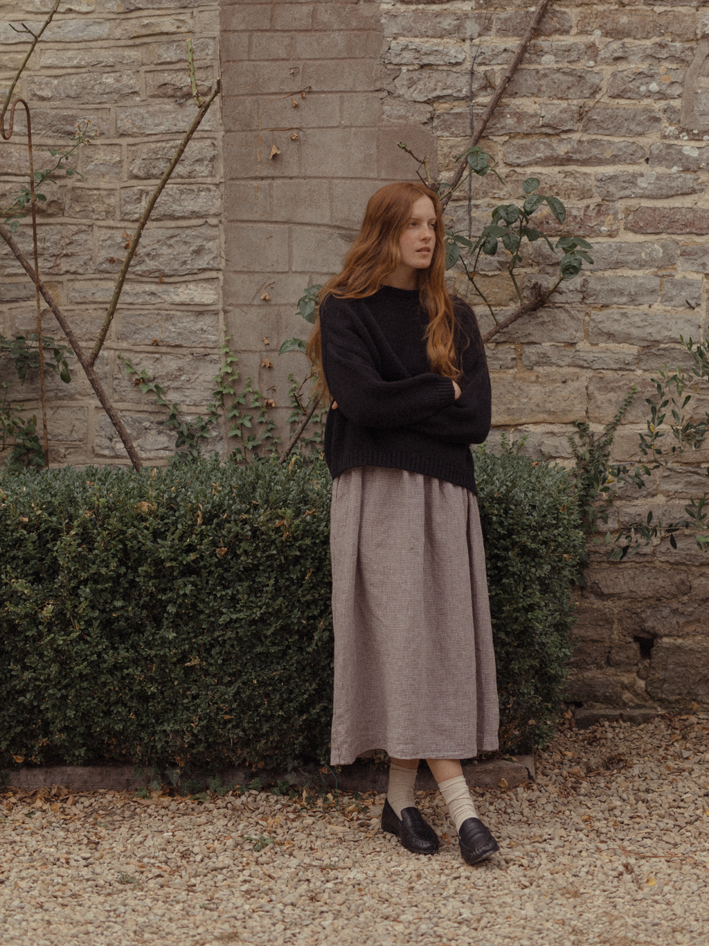 Model wearing the Townes Pullover in Noir by Gillian Stevens, styled with a midi skirt outdoors