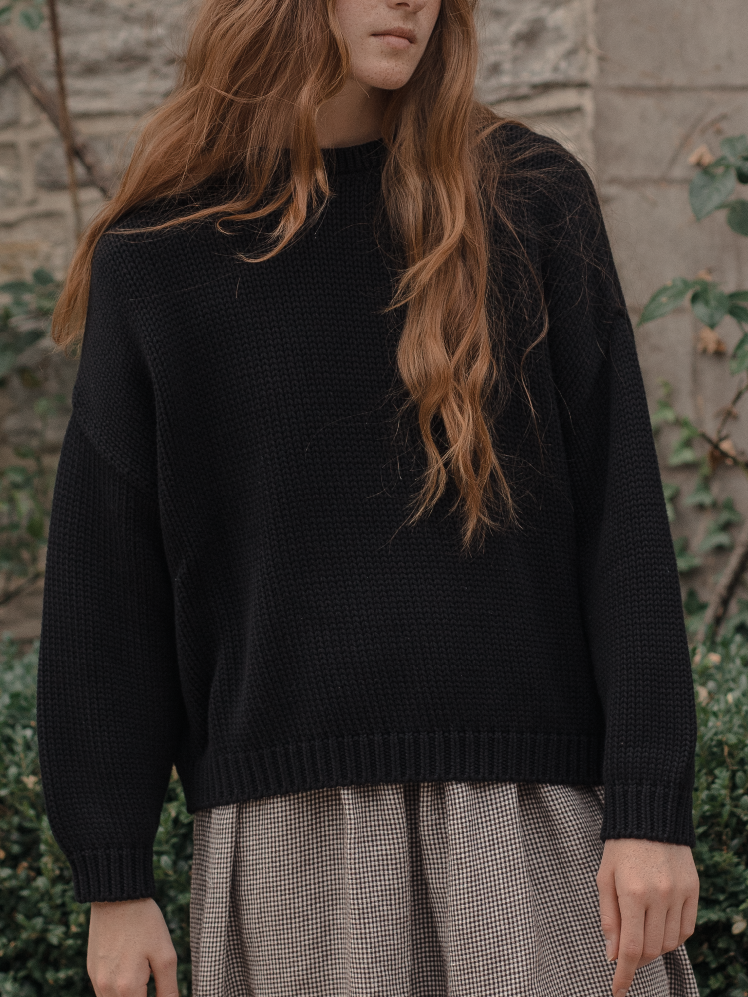 Model wearing the Townes Pullover in Noir by Gillian Stevens, front view styled over a check skirt