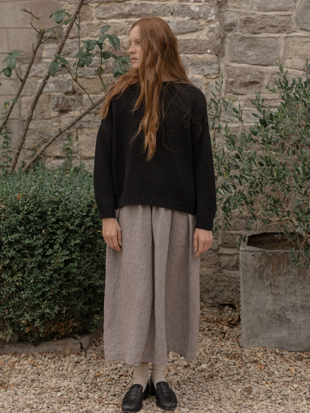 Model wearing the Townes Pullover in Noir by Gillian Stevens, three-quarter view in a stone courtyard