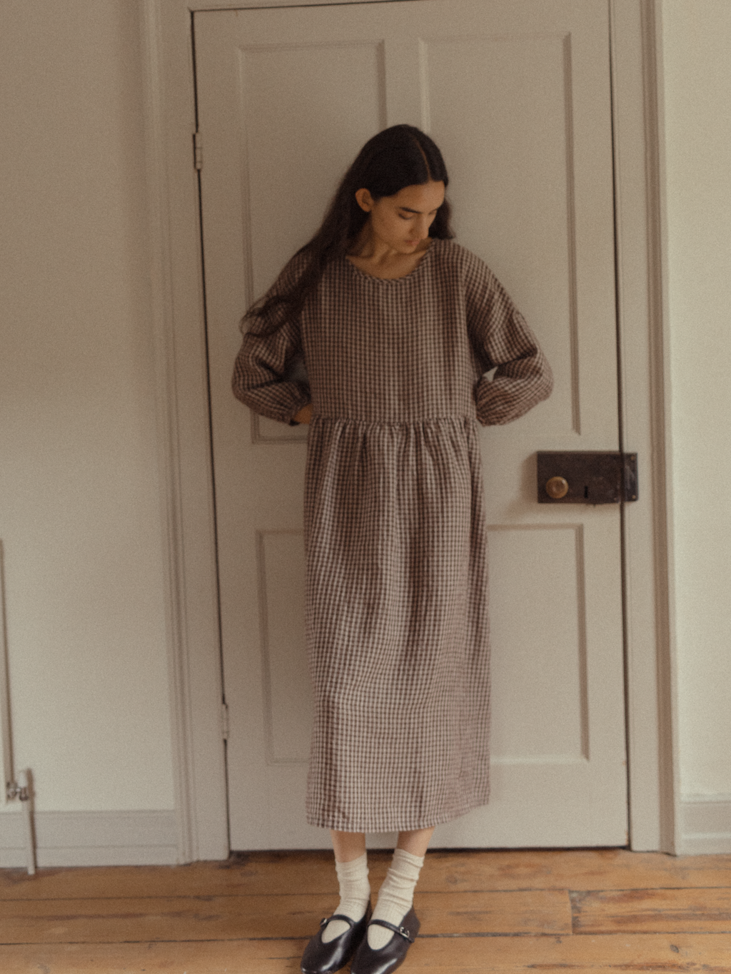 Model wearing the Darla Dress in Chocolate Plaid by Gillian Stevens, full-length front view in a heritage interior setting