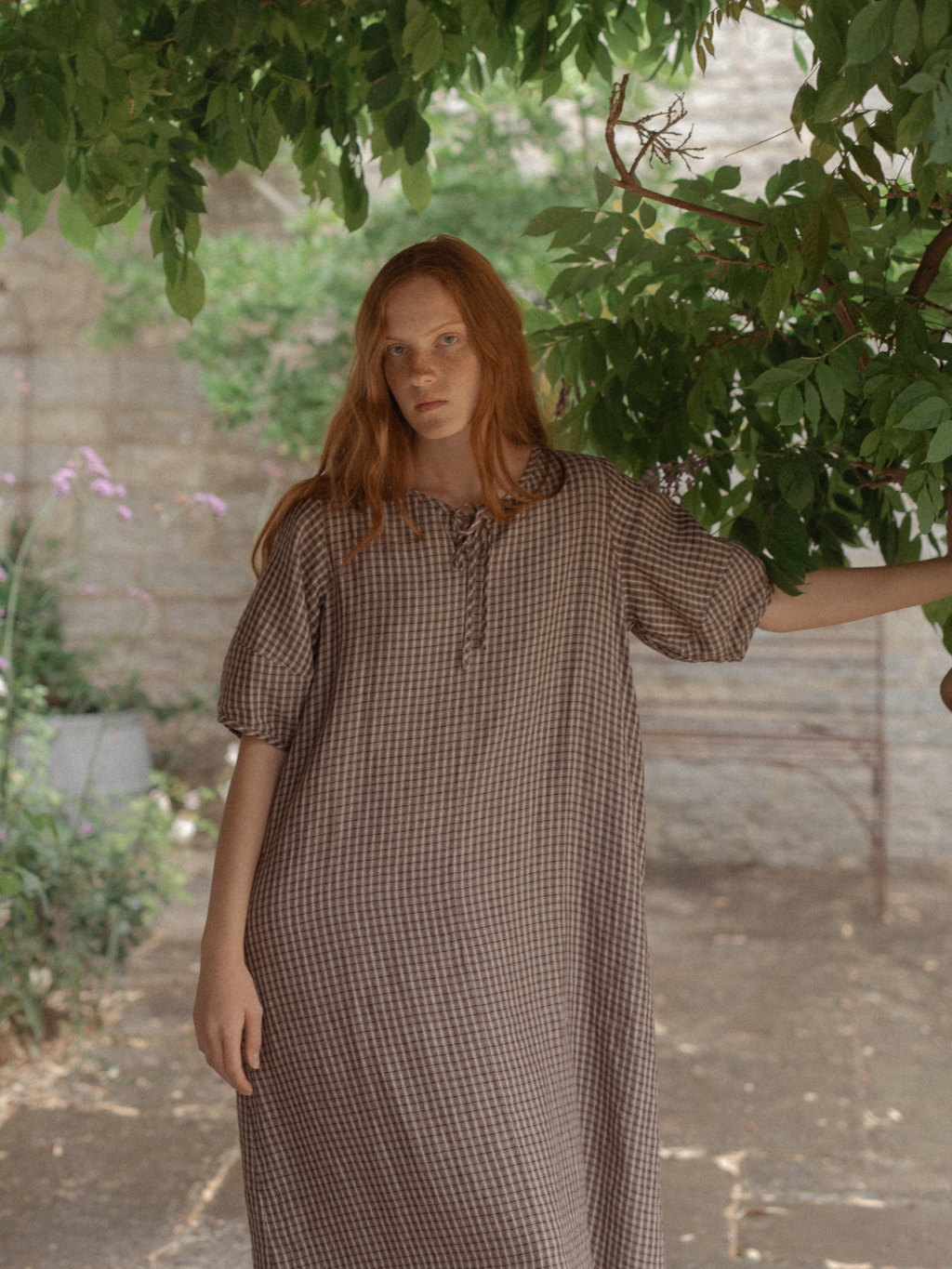 Model wearing the Blair Dress in Chocolate Plaid by Gillian Stevens, front view in a garden setting
