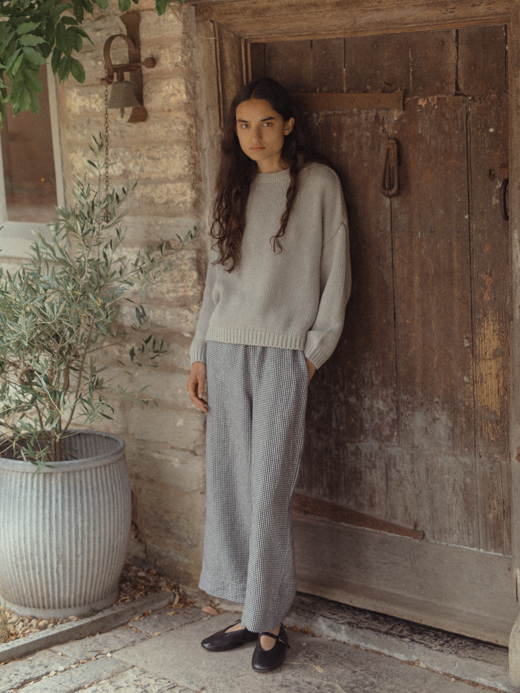 Model wearing the Townes Pullover in Pebble by Gillian Stevens, full-length front view against a rustic stone doorway
