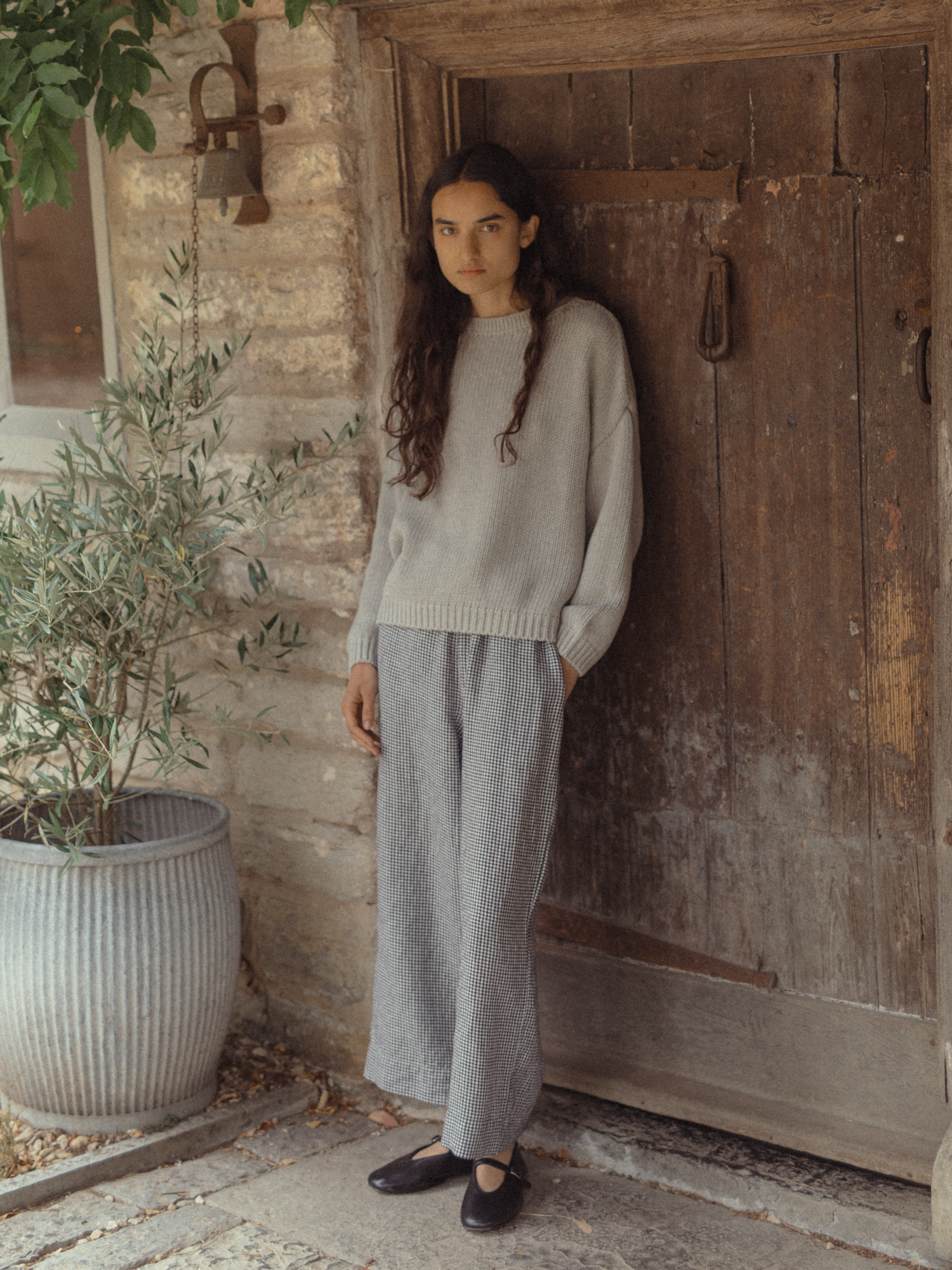 Model wearing the Townes Pullover in Pebble by Gillian Stevens, full-length front view against a rustic stone doorway