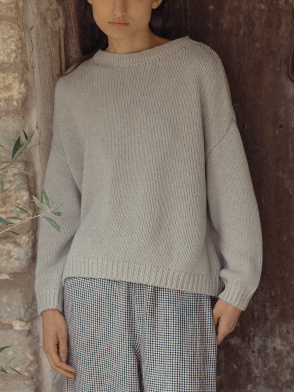 Model wearing the Townes Pullover in Pebble by Gillian Stevens, front view against a stone wall